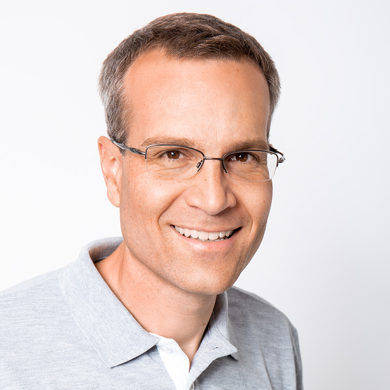 Porträt eines lächelnden Mannes (Dr. Moroni) mit Brille in einem grauen Polo-Shirt vor weißem Hintergrund.