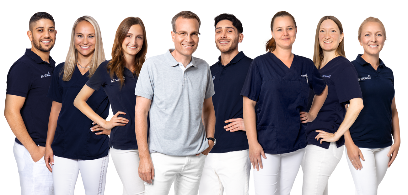 Team von MVZ Doktor Moroni lächelnd in Berufskleidung, weiß und dunkelblau, vor neutralem Hintergrund.