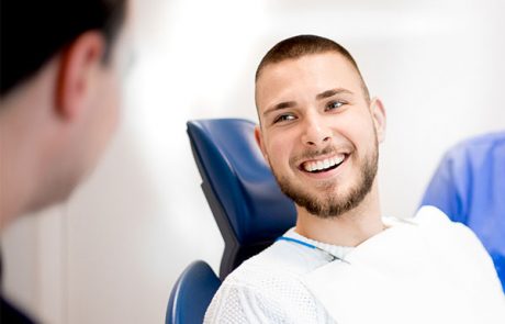 Ein lächelnder Mann im Zahnarztstuhl blickt zu seinem Zahnarzt auf, wobei nur der Rücken des Arztes sichtbar ist.